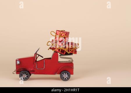 Altes rotes Auto mit Weihnachts- oder Neujahrsgeschenken isoliert auf einem beigen Hintergrund. Kreatives Minimal Holiday-Konzept. Stockfoto
