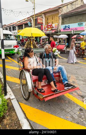 George Town, Penang, Malaysia - 1. Dezember 2019: Klassische lokale Rikscha mit Touristen bei bewölktem Wetter in Lebuh Armenische Straße, George Town, Penang Stockfoto