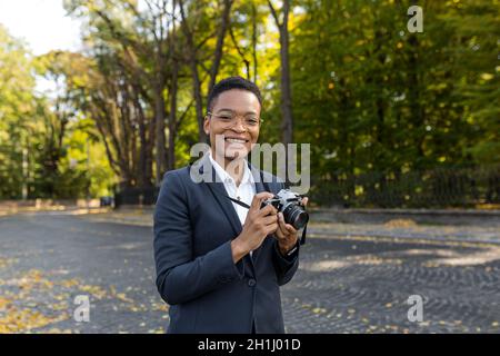 Überrascht und glücklich afroamerikanische Frau schaut auf die Kamera und lächelt mit einer Filmkamera auf einem Spaziergang im Park Stockfoto