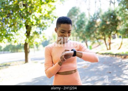 Die Sportlerin läuft morgens im Park, schaut auf das Fitness-Armband und freut sich über den Erfolg ihrer eigenen Ergebnisse Stockfoto