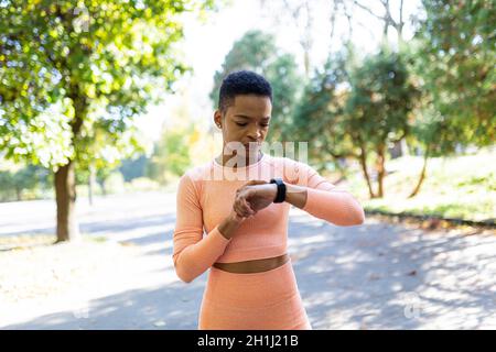 afroamerikanische Athletin wählt vor dem Training ein Fitnessprogramm auf einem Armband, im Herbstpark, einen gesunden aktiven Lebensstil Stockfoto