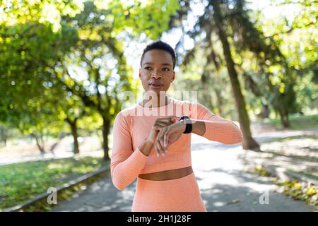 afroamerikanische Athletin wählt vor dem Training ein Fitnessprogramm auf einem Armband, im Herbstpark, einen gesunden aktiven Lebensstil Stockfoto