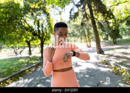 Die Sportlerin läuft morgens im Park, schaut auf das Fitness-Armband und freut sich über den Erfolg ihrer eigenen Ergebnisse Stockfoto