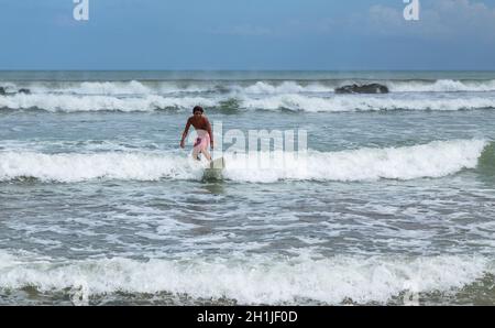 Bali, Indonesien - 17. September 2019: Surfer Mann am Sandstrand mit Surfbrett. Strand, Meer, heller sonniger Tag. Sommer-Lifestyle Stockfoto