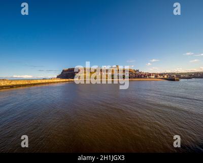 Die Ruinen der St Mary's Church und der Whitby Abbey befinden sich auf der East Cliff oberhalb der Cottages der Henrietta Street mit dem Hafen im Vordergrund. Whitby, North Yorkshire, Großbritannien Stockfoto