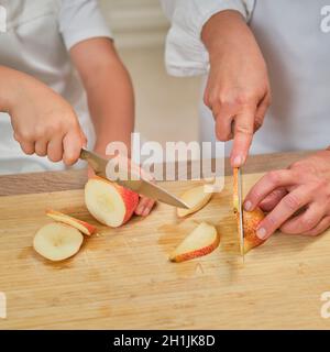 Mutter und Sohn in weißen Chefkleidern schnitten in ihrer eigenen Küche mit einem Messer Birnen. Eine Erwachsene Frau mit einem kleinen Jungen wird einen Kuchen kochen Stockfoto