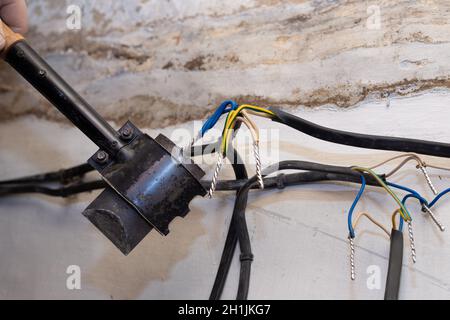 Ein Elektriker löt verdrehte elektrische Drähte in einem Haus im Bau. Anschluss und Verdrehen der Kabel. Stockfoto