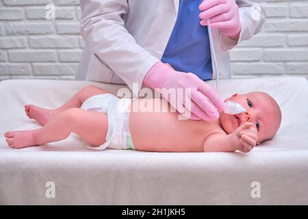 Der Arzt entfernt bei einem Neugeborenen eine laufende Nase mit einer Absaugvorrichtung. Krankenschwester in Uniform behandelt Kindernase für Grippe Stockfoto