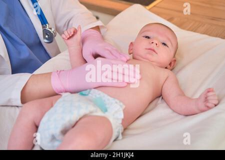 Der Arzt macht Gymnastik und massiert ein neugeborenes Baby. Krankenschwester in Uniform, die dem Kind Aufwärmübungen macht Stockfoto
