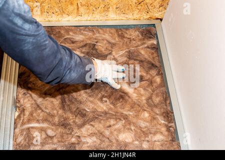 Der Arbeiter dämmelt die Wände mit Mineralwolle zur weiteren Verkleidung mit Gipskarton. Wärmedämmung und Schalldämmung des Hauses. Stockfoto