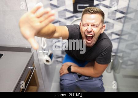 Ein junger Mann schreit, während er in der Nähe auf der Toilette sitzt Stockfoto