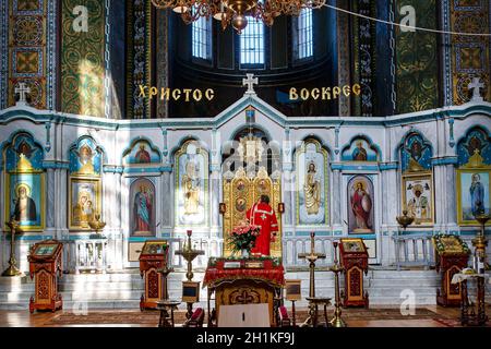 Orthodoxe christliche Kirche im Inneren. Blick auf die Ikonostase mit Ikonen und Priestern in roten Kleidern. Die Inschrift auf Russisch ist Christ Risen. Osterfest Stockfoto