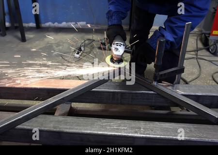 Schleifen von Metall.Schleifscheibe. Der Schlosser reinigt die Eisenkecke nach dem Schweißen in der Werkstatt. Funken fliegen. Stockfoto