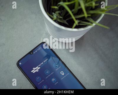 LOD, Israel - 8. Juli 2020: Moderner minimalistischer Büroarbeitsplatz mit schwarzem Smartphone mit Israel Railways App Launch Screen mit Logo auf hebräisch Stockfoto