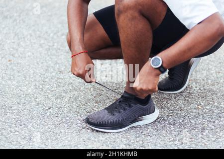 Nahaufnahme Asian Sport Läufer schwarz Mann tragen Uhr sitzend er versuchen Schnürsenkel Laufschuhe immer bereit zum Joggen und laufen auf der Straße im Freien heilen Stockfoto