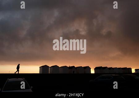 AJAXNETPHOTO. DEZEMBER 2020. WORTHING, ENGLAND. - REGENWOLKEN - FEUCHTIGKEITSBELADENE STRATUS WOLKEN TREIBEN ÜBER STRANDHÜTTEN UND EIN WALKER AM MEER BEI SONNENUNTERGANG.FOTO:JONATHAN EASTLAND/AJAX REF:GR202212 9921 Stockfoto