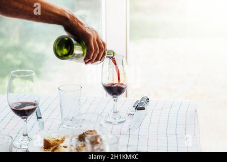 Die Hand eines Mannes, der Wein in ein Glas gießt. Familientisch in Argentinien an einem Sonntagmittag mit Grill. Stockfoto