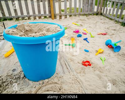 Weitwinkel-Nahaufnahme in einem eingezäunten Sandkasten an der deutschen Nordseeküste mit blauen Sandeifern im Vordergrund und Sandgrabspielzeug für Kleinkinder Lyi Stockfoto