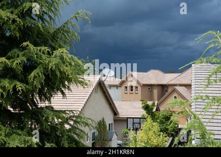 Auf dem Dach eines Vorstadthauses mit riesigen Sturmwolken am Himmel erscheint eine Einzelschüssel-Satellitenschüssel. Stockfoto