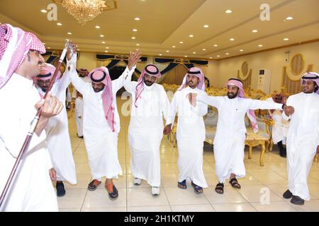 2020. Juli, Hochzeitssaal Riad, Saudi-Arabien, Saudi-arabische Männer feiern und genießen traditionellen Tanz mit kulturellen Objekten in den Händen während der Hochzeit Veranstaltung Stockfoto