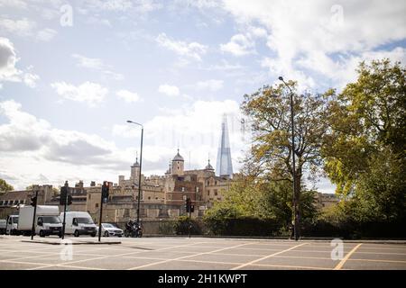 Bild von zwei Lieferwagen, einem Auto und einem Motorrad hielten auf der Straße neben einem Baum, unter einem leicht bewölkten Himmel und mit dem Tower of London und dem Stockfoto
