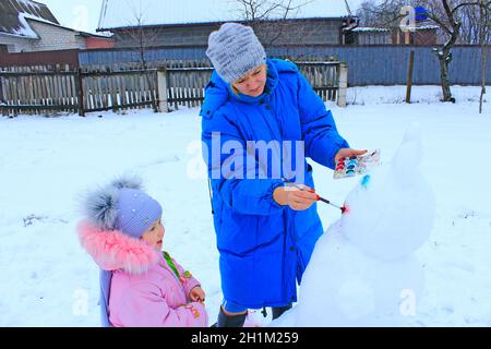 Mutter malt Schneemann. Winterurlaub genießen. Familienurlaub im Winter. Attribut „Neues Jahr“. Familienurlaub im Winter. Frau zeichnet Lächeln für New Y Stockfoto