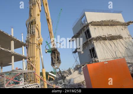 Betonschutt und hängende Stahlseile auf dieser Abrissstelle, großer, hoch reichender Abrissbagger im Vordergrund, mit Turmkran dahinter Stockfoto