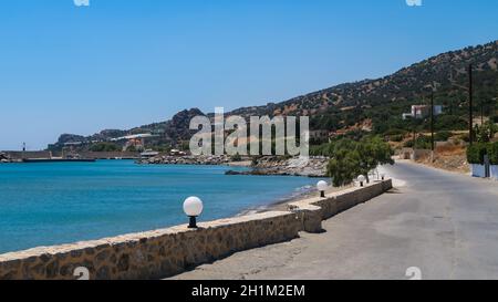 Straße und Meer in Keratokampos, Kreta mit einem kleinen Hafen und Olivenbäumen auf dem Berg Stockfoto