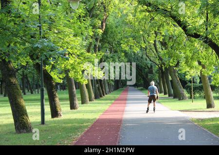 Wunderschöner Stadtpark mit Laufband und Mann, der auf Rollschuhe läuft. Alter Mann läuft auf Rollerskates im Stadtpark. Urbane Natur. Gesunde Lebensweise Stockfoto