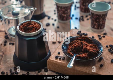 Zerlegte Kaffeemaschine und ein Teller mit gemahlenem Kaffee auf einem Tisch, umgeben von Kaffeesachen Stockfoto