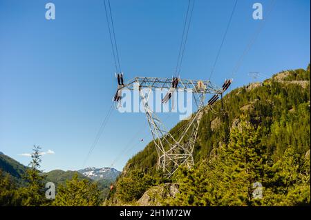 Stromleitungen und Turm, die durch Wald und Berge gegen klaren blauen Himmel in British Columbia, Kanada. Stockfoto