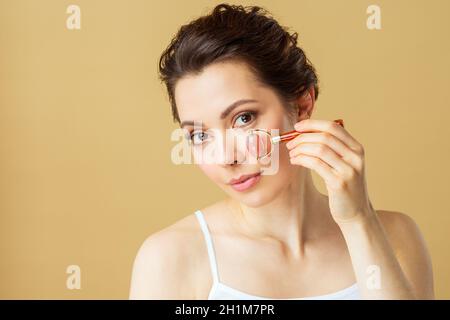 Porträt einer jungen Frau mit einer Gesichtsmassagerolle aus natürlichem Rosenquarz. Stockfoto