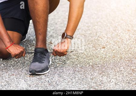 Nahaufnahme Asian Sport Läufer schwarz Mann tragen Uhr sitzen er versuchen Schnürsenkel Laufschuhe immer bereit für Joggen und laufen Outdoor Straße Gesundheitspark Stockfoto