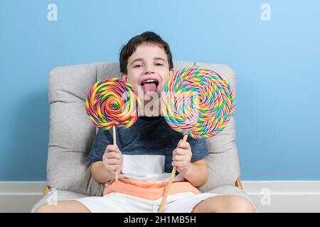 Der 8-jährige Brasilianer hält zwei große Lutscher und ragt seine Zunge heraus. Stockfoto