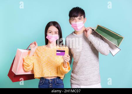 Junges Paar trägt Winterkleidung mit medizinischer Maske, die Einkaufstaschen und Kreditkarten hält.isoliert auf blauem Hintergrund. Stockfoto