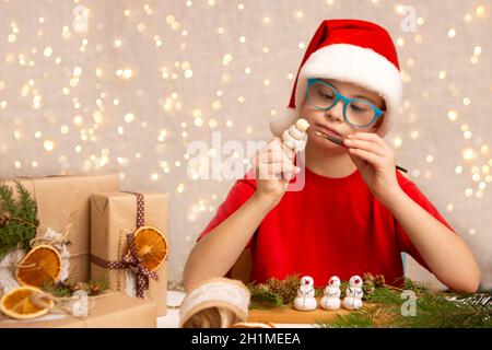 Ein Mädchen mit Down-Syndrom malt einen Schneemann aus Teig, um einen Weihnachtsbaum zu schmücken Stockfoto