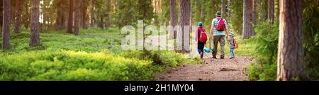 Vater und Jungen gehen Camping mit Zelt in der Natur. Mann mit Söhnen und Rucksäcken, der im Wald spazierengeht Stockfoto
