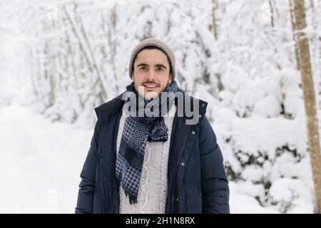 Europäischer Mann, der lächelnd im Winterwald steht. Verschneite Wintertage. Lächelnder Mann Stockfoto