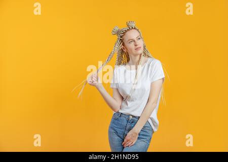 Kaukasische junge blonde Frau träumt und verdreht Haare um die Finger, korrigiert isolierten gelben Hintergrund Stockfoto