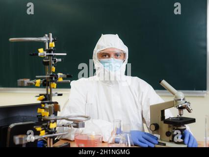 Ein Chemiker in einem Schutzanzug sitzt in seinem Labor, es gibt eine Menge chemischer Ausrüstung. Stockfoto
