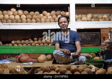 Der indische Verkäufer sitzt im New Market in Kalkata hinter einem großen Stapel von gehäuteten braunen Kokosnüssen Stockfoto