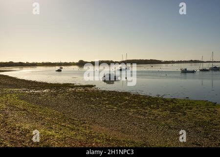 Boote vertäuten am Dell Quay in Chichester Harbour, West Sussex, England. Mit klarem blauen Himmel und flachem, ruhigem Wasser. Stockfoto
