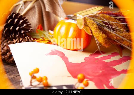 Roter Hand-pute auf Vanille-Baupapier, in Orange gerahmt, mit orangefarbenen Beeren, Kiefernblättern, einem kleinen orangefarbenen Kürbis und braunem Laub Stockfoto