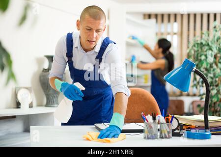 Qualifizierte Hausmeister Staubwischen Möbel im Büro mit Reinigungsgeräten Stockfoto