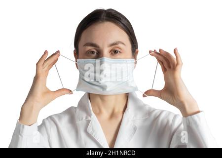 Nette Ärztin, Krankenschwester setzt auf eine medizinische Gesichtsmaske, Atemschutzmaske. Schöne Ärztin zeigt, wie man eine auf weißem Rücken isolierte Schutzmaske aufsetzt Stockfoto