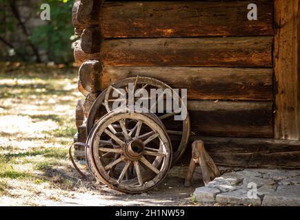 Holzräder von einem alten Wagen vor stehen Die Wand eines hölzernen Landhauses Stockfoto