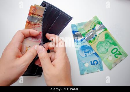 Eine Person, die eine Brieftasche öffnet und kanadische Dollar auf weißem Hintergrund ausgibt. Konzept: Geld Ausgeben Stockfoto