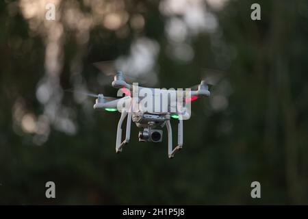 Fliegende Quad Copter UAV Drohne schwebend mit unfokussierter Baum Hintergrund. Aufgenommen während der goldenen Stunde am Abend bei Sonnenuntergang. Stockfoto