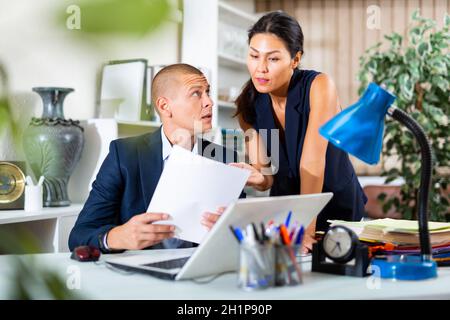 Geschäftsmann mit Partnerin, die am Schreibtisch am Laptop arbeitet Stockfoto