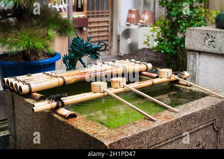 Pavillon für Wasseraufbereitungen für eine zeremonielle Reinigung im Nishiki Tenmangu-Schrein, Kyoto, Japan. Quelle natürliches Wasser fließt aus dem Untergrund. Stockfoto